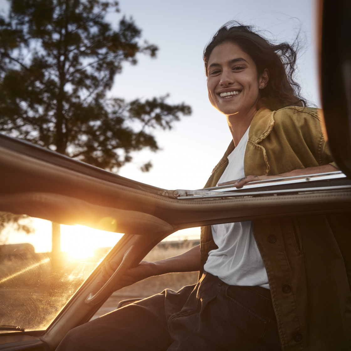 Happy young woman hanging out of the car window